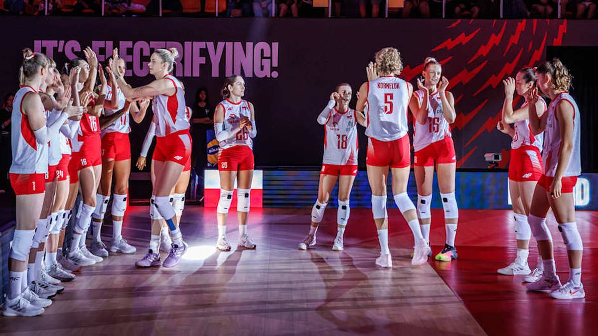 Polskie siatkarki stoją w rzędzie na boisku, zwr&oacute;ceni do siebie, prawdopodobnie podczas przerwy w meczu. Na ich strojach widnieją biało-czerwone barwy.