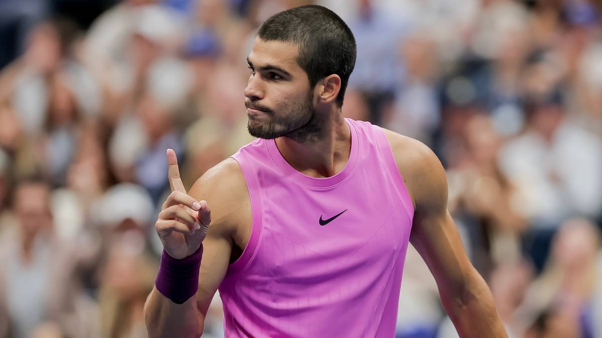 Carlos Alcaraz, tenisista w różowej koszulce, podnosi palec wskazujący w górę, patrząc w bok.