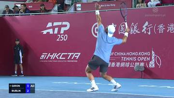 Gracz w niebieskiej koszulce i czarnych spodenkach wykonuje serwis podczas meczu tenisowego.