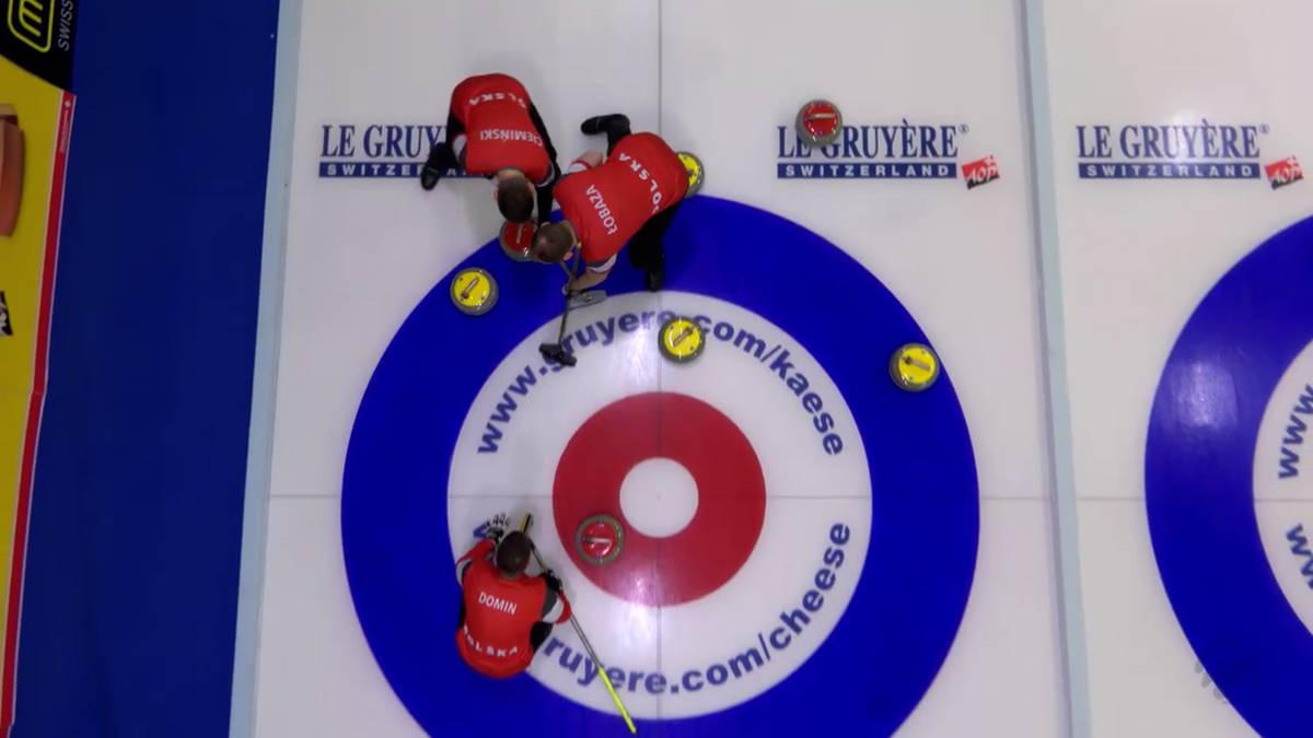 Gracze w curlingu w czerwonych strojach wykonują rzut kamieniem na lodowisku, celując w tarczę.