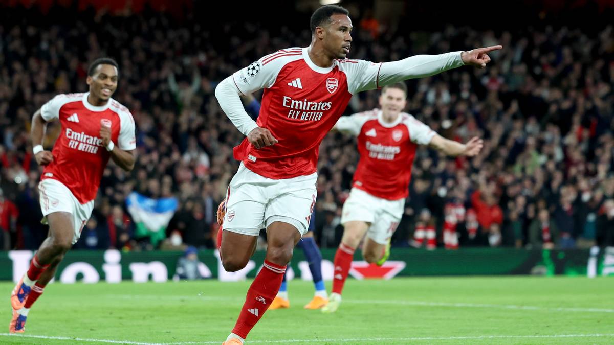 Piłkarze w czerwonych koszulkach z białymi rękawami i białymi spodenkami biegną po zielonej murawie stadionu. Jeden z nich, wskazujący palcem w prawo, cieszy się z bramki.