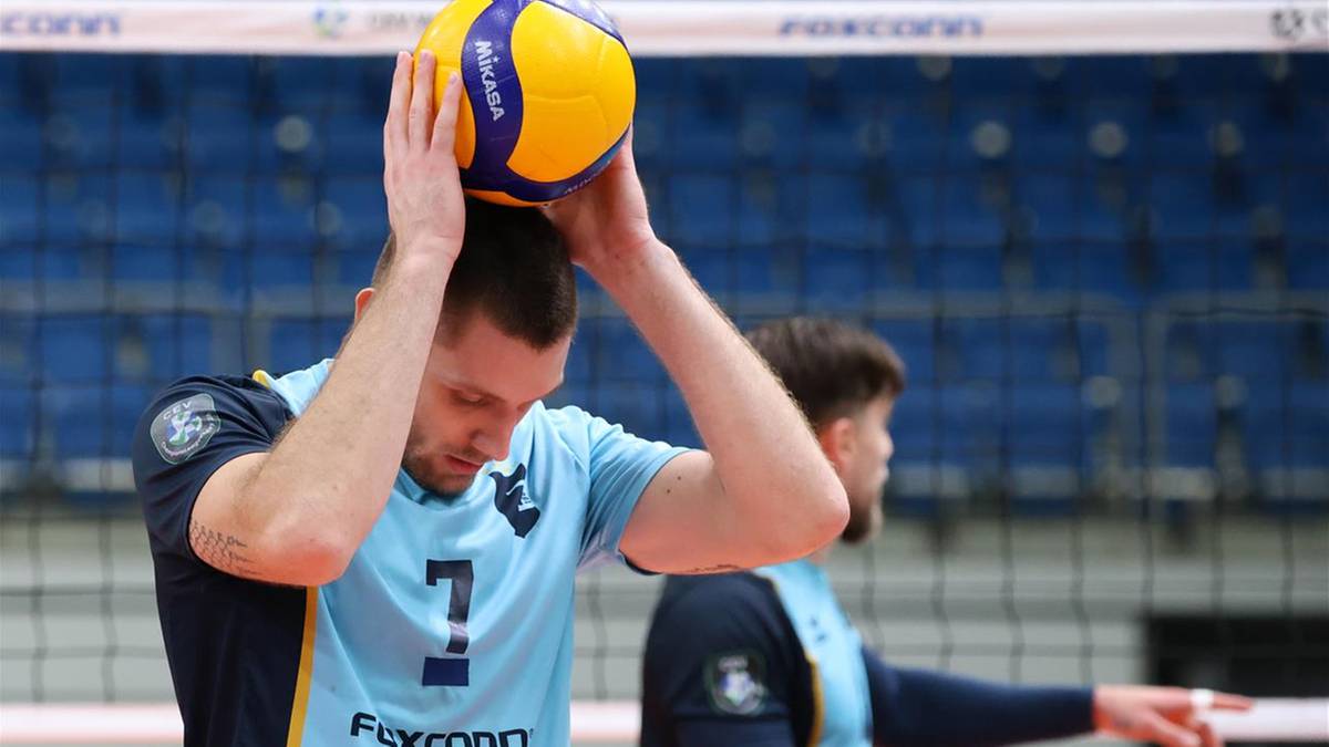 Siatkarz trzyma piłkę do siatk&oacute;wki nad głową.