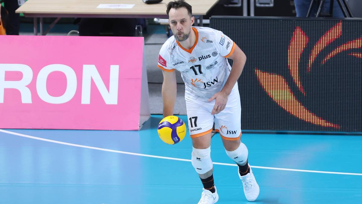 Siatkarz w białej koszulce z numerem 17 i białych spodenkach prowadzi piłkę do siatk&oacute;wki na boisku.