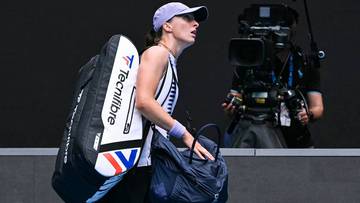 Tenisistka z torbą sportową idzie po korcie, w tle kamerzysta z kamerą.