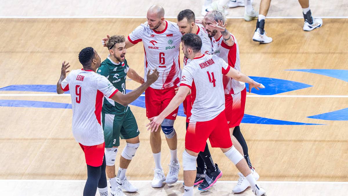 Siatkarze w białych i zielonych strojach sportowych rozmawiają ze sobą na parkiecie.