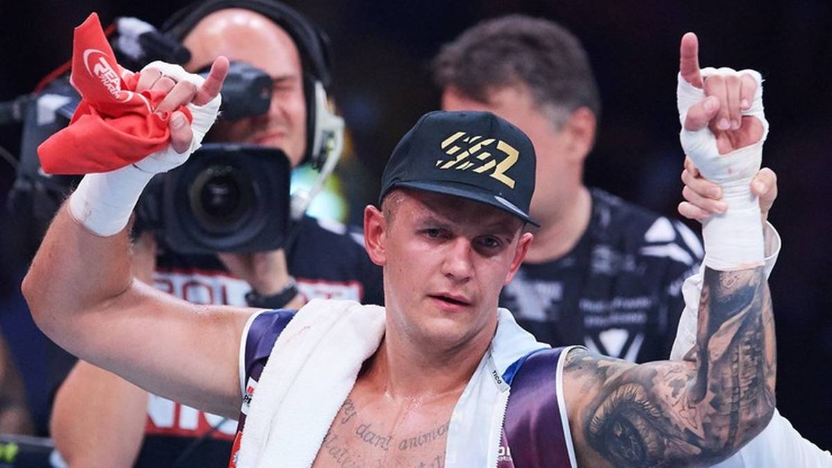 Bokser z uniesionymi rękami w geście zwycięstwa, z czerwoną chusteczką w dłoni.