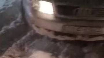 Samoch&oacute;d osobowy częściowo widoczny z przodu, stojący w gęstej, brązowej pianie na drodze. Śnieg jest mokry i tworzy duże hałdy.