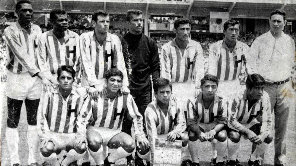 Drużyna piłkarska w strojach w paski, pozująca do zdjęcia na tle trybun stadionu.