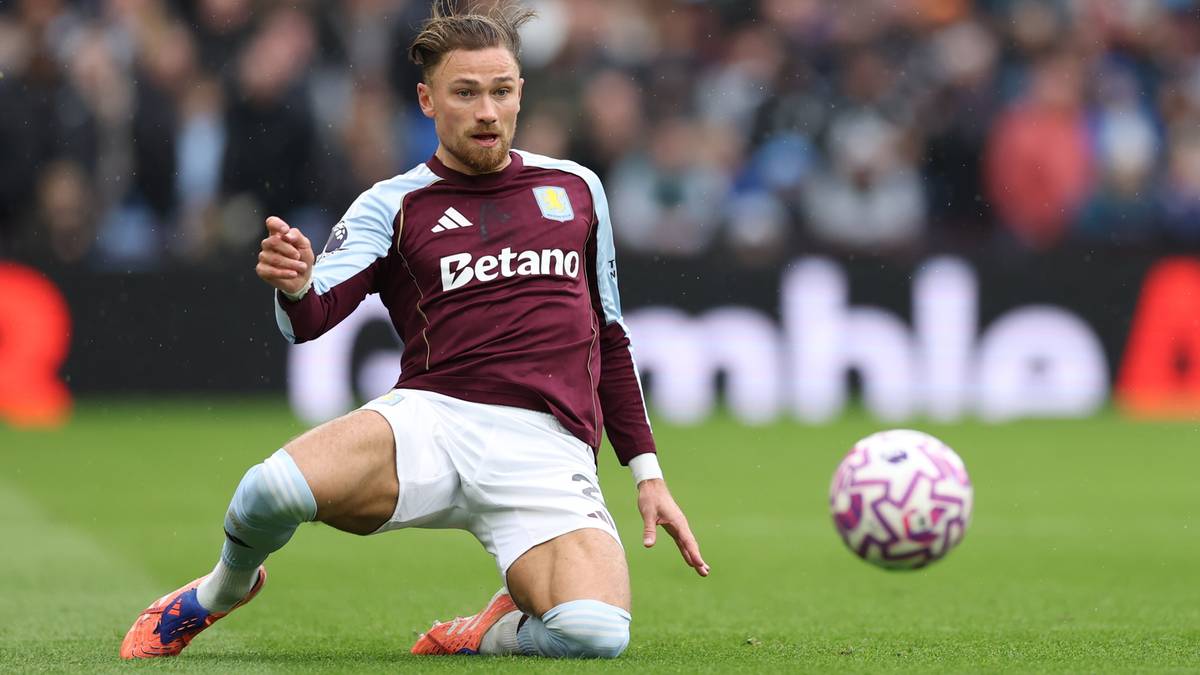 Piłkarz w bordowej koszulce i białych spodenkach na boisku, z piłką obok.