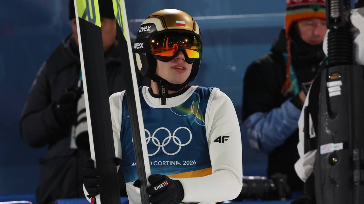 Skoczek narciarski w złotym kasku i goglach narciarskich trzyma narty.