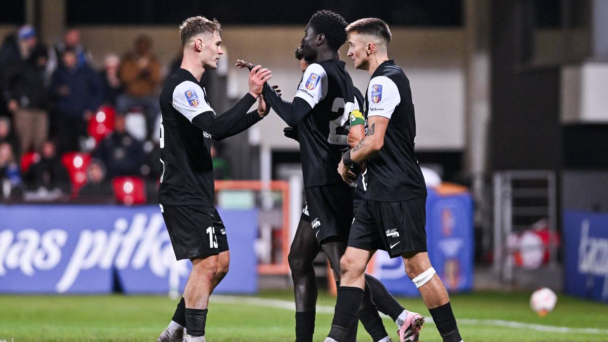 Trzech piłkarzy w czarnych strojach świętuje razem na boisku.