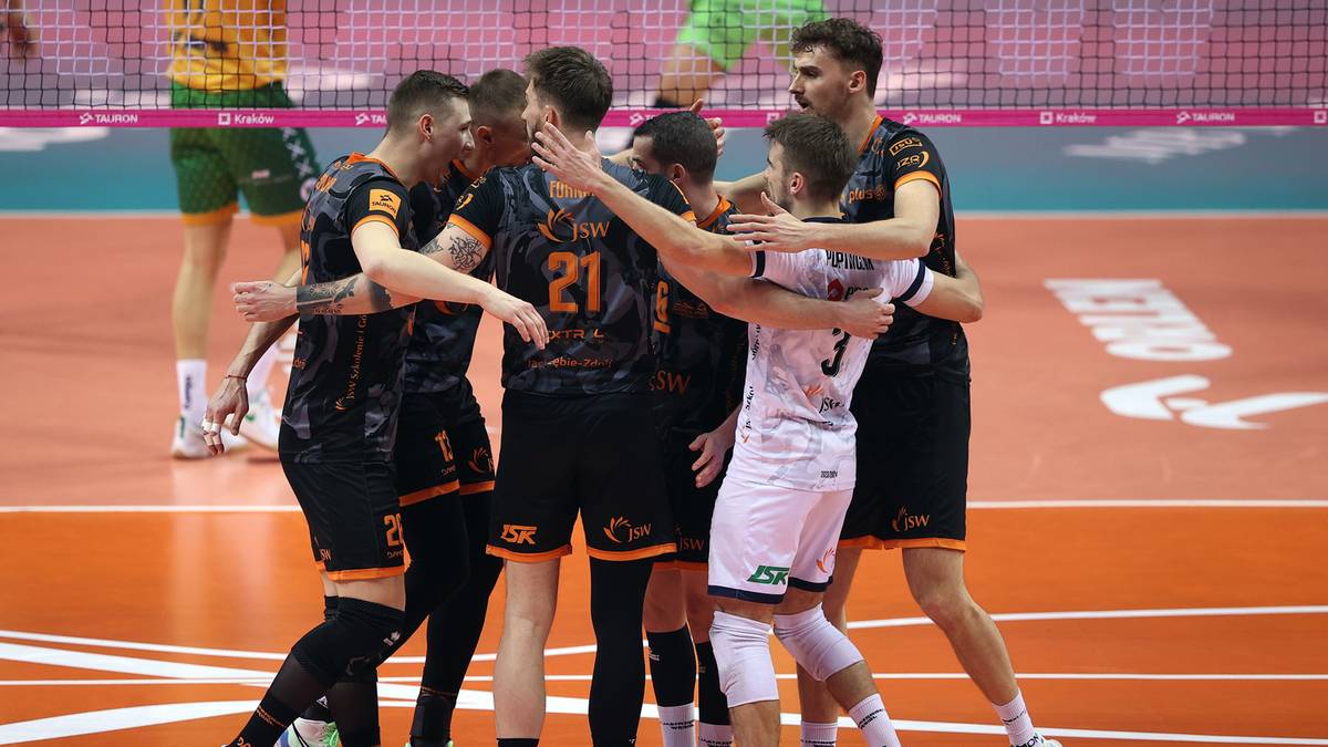 Drużyna siatkarzy świętująca na boisku, otaczając się nawzajem w geście radości.