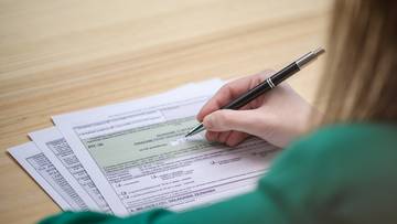 Dłoń osoby piszącej długopisem na dokumencie podatkowym.