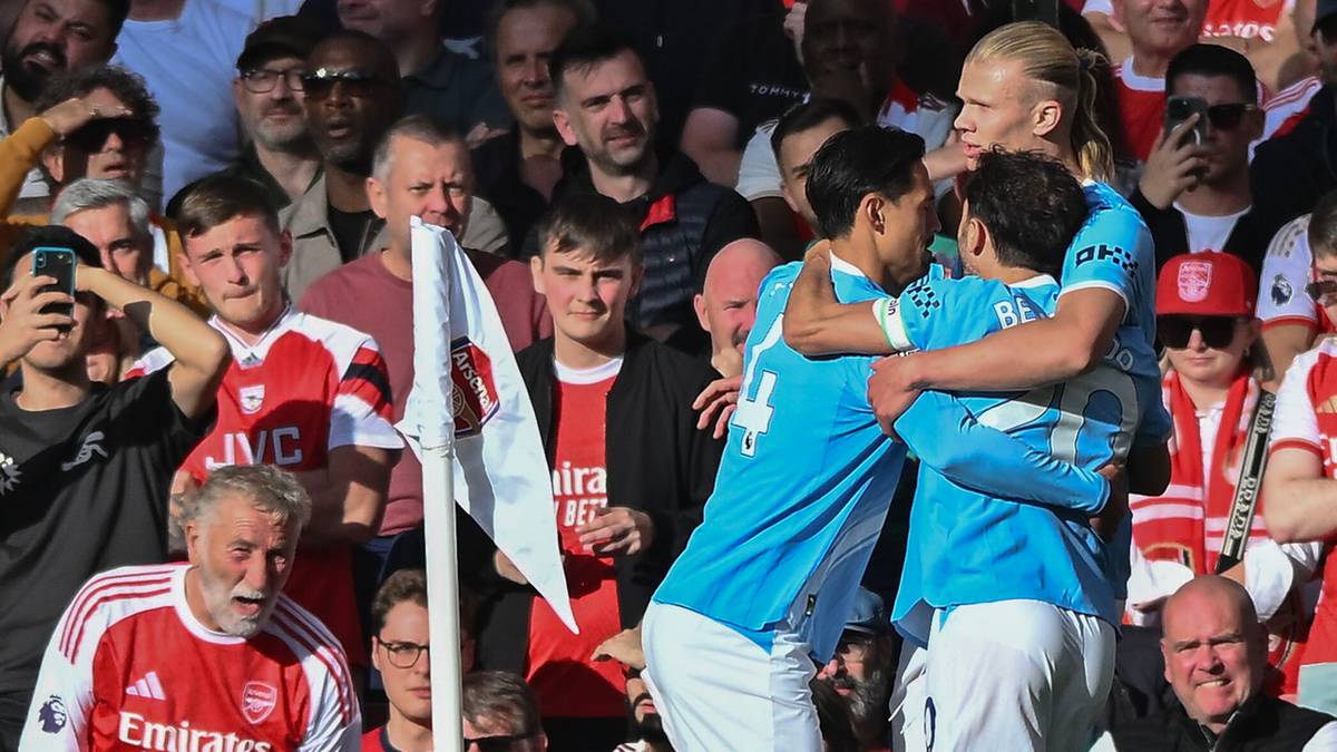 Piłkarze w niebieskich strojach, świętujący zdobycie gola lub zwycięstwo, są otoczeni przez kibiców w białych i czerwonych strojach na stadionie.
