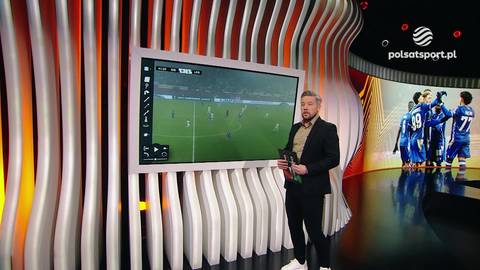 Dariusz Rolak, dziennikarz sportowy, stoi obok dużego ekranu z widokiem na boisko piłkarskie podczas analizy meczu Sigma Ołomuniec - Lech Poznań.