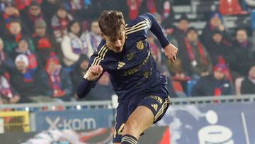 Piłkarze drużyny w żółtych strojach próbują odebrać piłkę zawodnikowi w granatowym stroju.