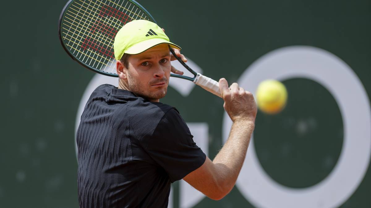 Hubert Hurkacz, tenisista, podczas meczu, w żółtej czapce i czarnym stroju, uderza piłkę rakietą.