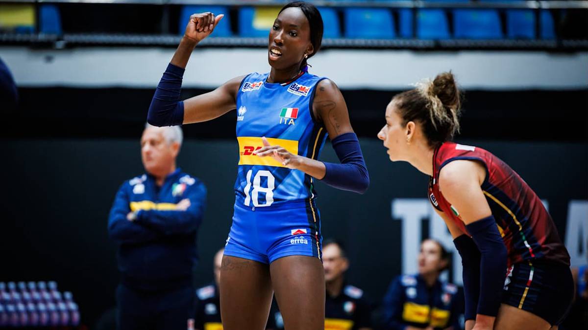 Siatkarka w niebieskim stroju z numerem 10, uniesioną ręką, na tle innego zawodnika i trybun.