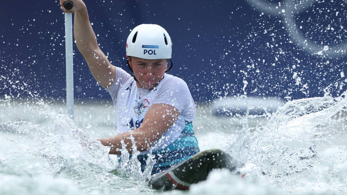 Zawodniczka w białym kasku z napisem "POL" wiosłuje kajakiem, rozbijając wodę.