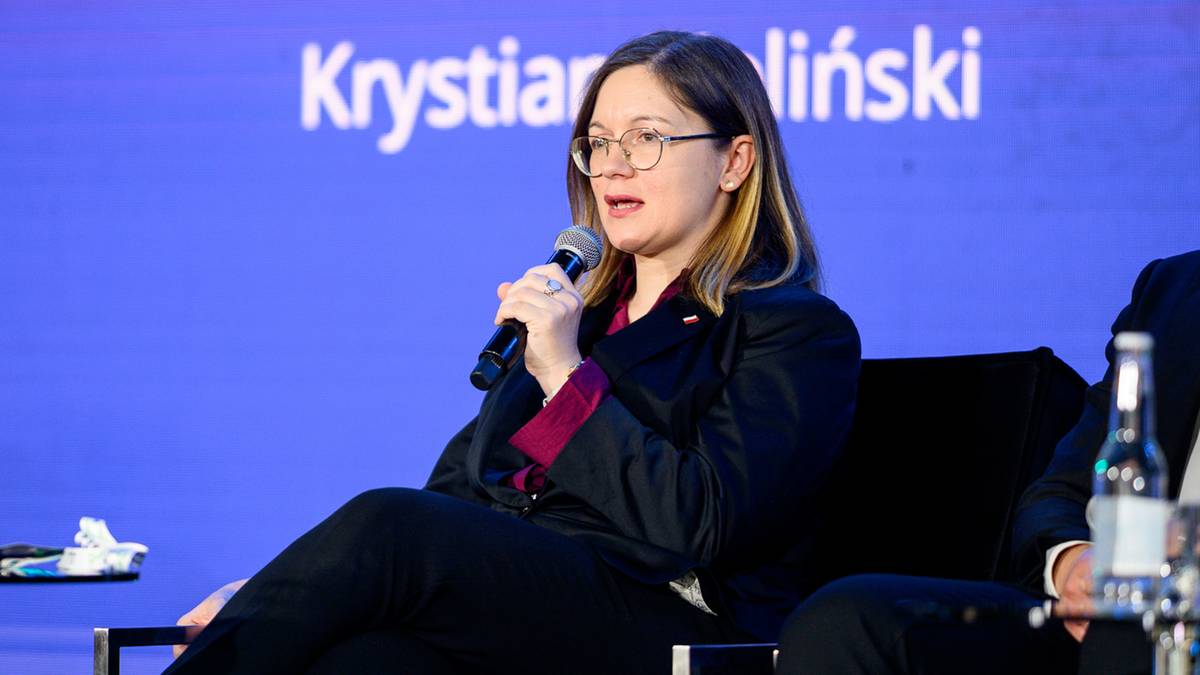 Kobieta w okularach siedzi i mówi do mikrofonu, na niebieskim tle z napisem Krystian i liński