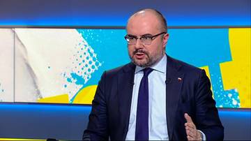 Mężczyzna w garniturze i krawacie, m&oacute;wiący do kamery. Ma okulary i zarost.