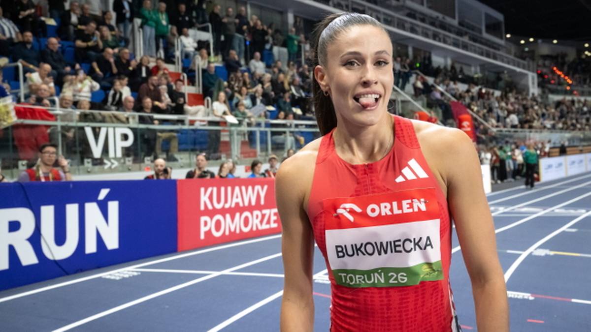 Lekkoatletka z nazwiskiem Bukowiecka na stroju sportowym z logo ORLEN, stojąca na bieżni lekkoatletycznej w hali, z kibicami na trybunach w tle.