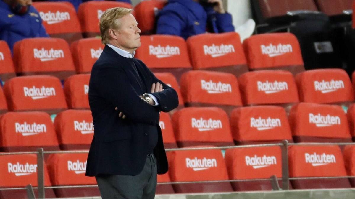 Ronald Koeman stoi ze skrzyżowanymi rękami na tle pustych czerwonych siedzeń.