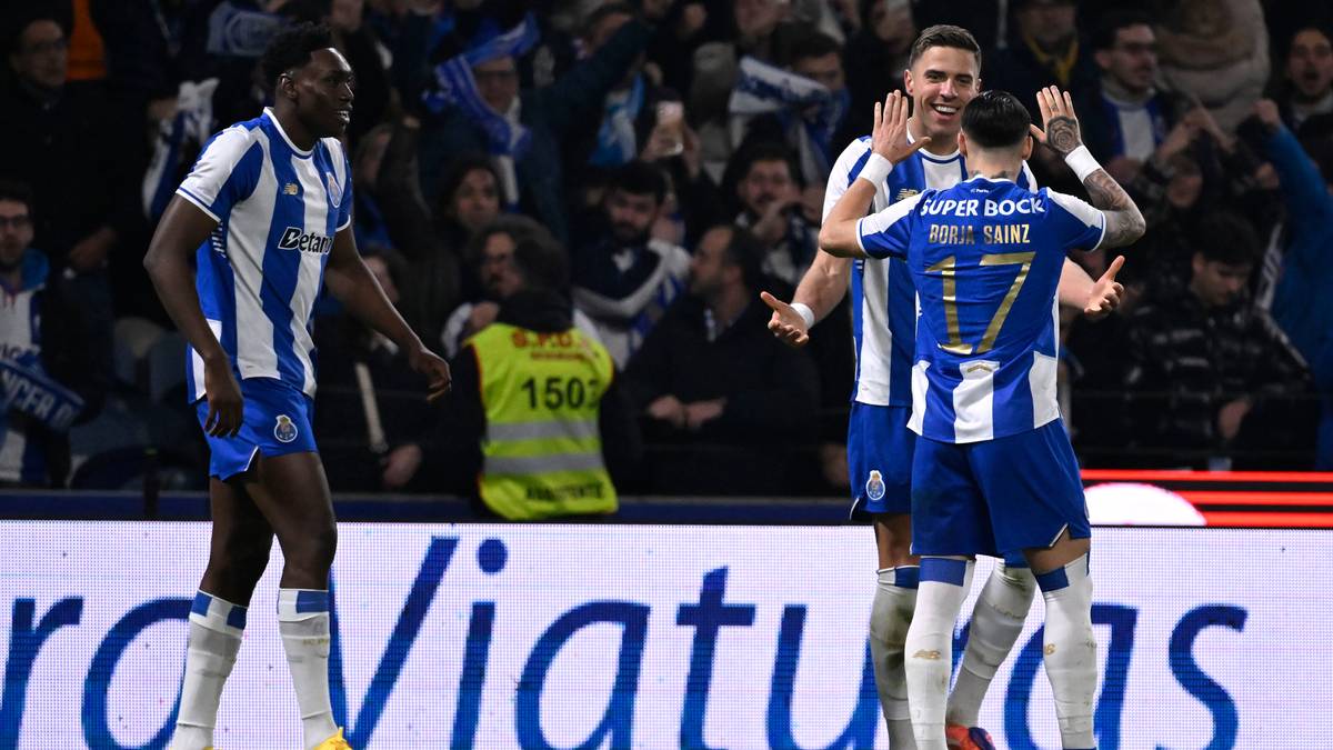 Trzech piłkarzy w niebiesko-białych strojach świętuje bramkę na tle trybun stadionu.