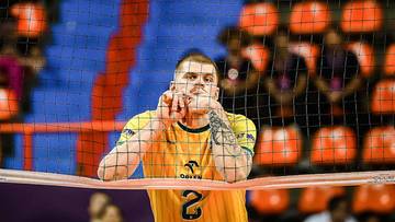 Siatkarz w ż&oacute;łtej koszulce z numerem 2 na plecach, z rękami przy twarzy, stoi przy siatce.