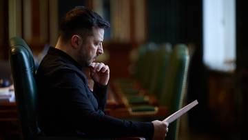 Prezydent Ukrainy Wołodymyr Zełenski siedzi w fotelu, czytając dokument.
