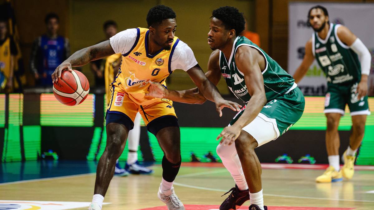 Dw&oacute;ch koszykarzy w akcji podczas meczu, jeden w ż&oacute;łtej koszulce z piłką, drugi w zielonej koszulce go broni.