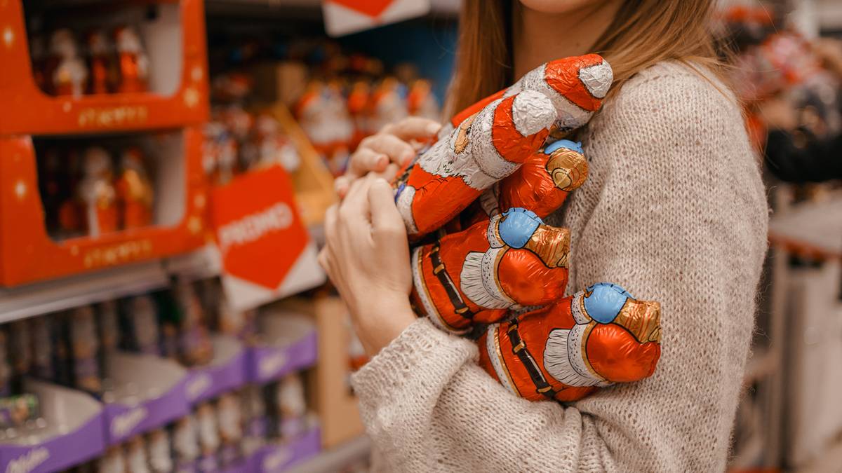 Dłoń trzyma czekoladowe figurki św. Mikołaja opakowane w czerwono-biały papier.