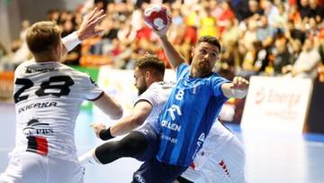 Zawodnicy piłki ręcznej podczas meczu, jeden z nich rzuca piłkę do bramki, podczas gdy inni próbują go zatrzymać.