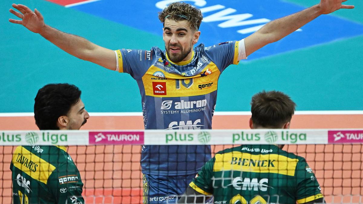 Siatkarz w niebiesko-żółtym stroju z otwartymi ramionami, dwóch innych zawodników w zielonych strojach obok.