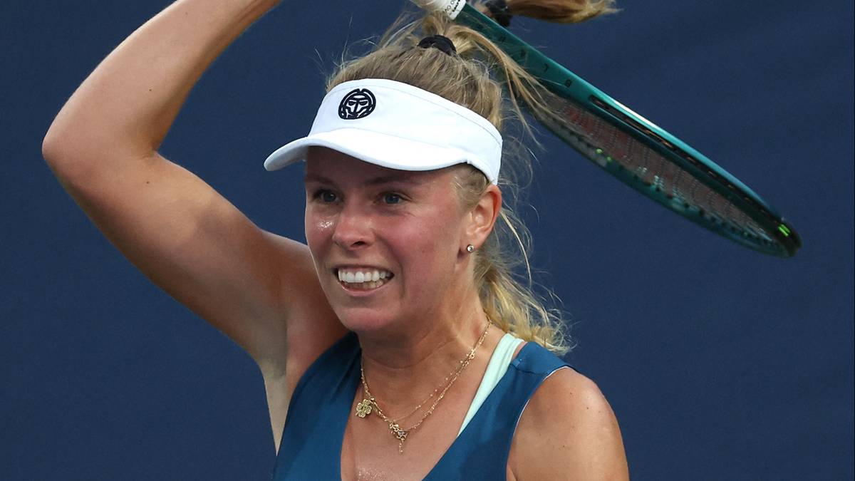 Kobieta w białej czapce z daszkiem i sportowym topie gra w tenisa na US Open, z rakietą tenisową nad głową.