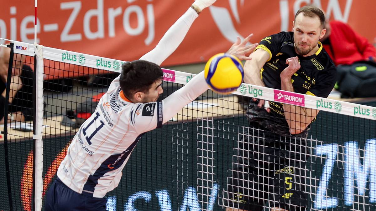 Siatkarz wykonuje atak blokowany przez przeciwnika przy siatce podczas meczu.