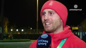 Damian Żurek w czerwonej czapce i bluzie, trzyma mikrofon Polsat Sport, udziela wywiadu.