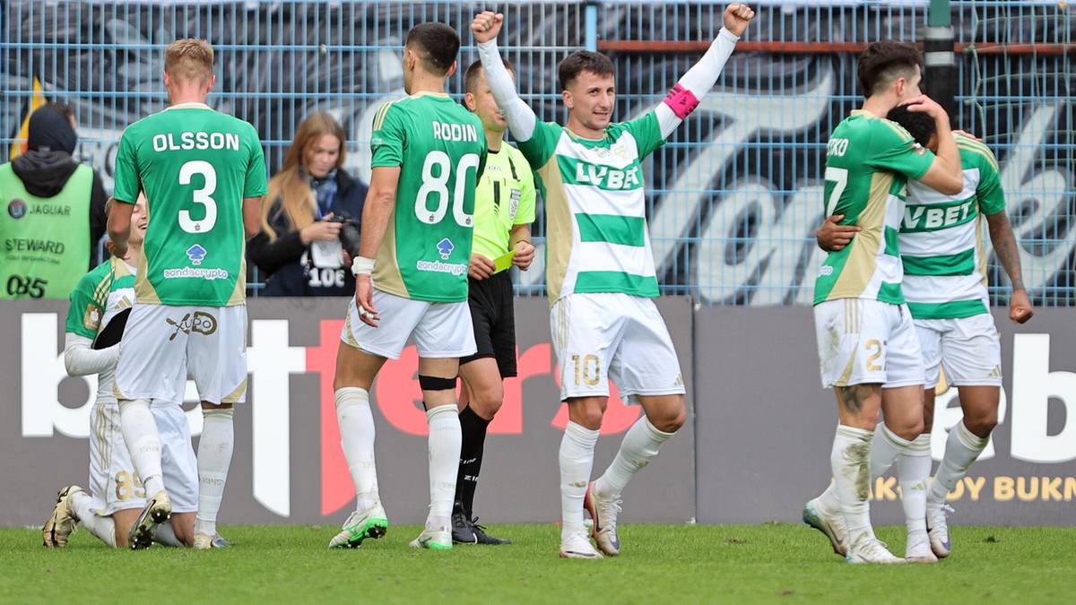 Piłkarze Lechii Gdańsk w zielono-białych strojach świętują zdobytego gola po doliczonym czasie gry. Jeden z zawodników unosi ręce w geście triumfu.