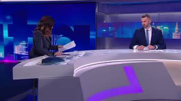 Marcin Możdżonek siedzi przy stole w studiu telewizyjnym, ubrany w garnitur i krawat, rozmawiając z kobietą po drugiej stronie stołu.