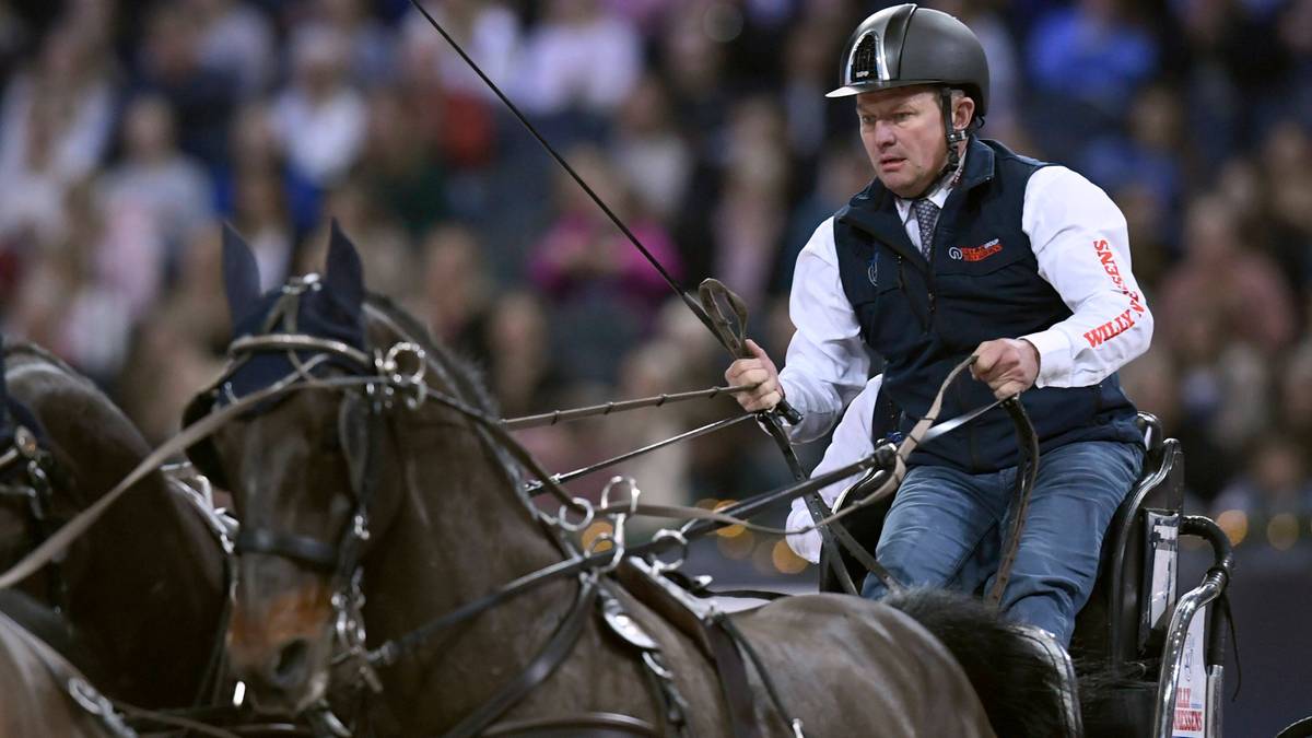 Mężczyzna w kasku prowadzi zaprzęg czterokonny podczas zawodów.