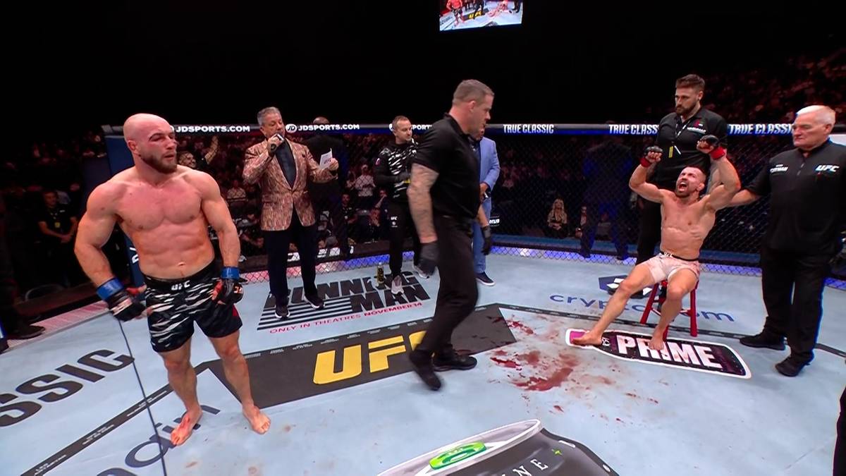 Dwóch zawodników MMA w oktagonie. Jeden zawodnik z podniesionymi rękami siedzi na krześle, podczas gdy drugi stoi obok. Na podłodze widać krew.