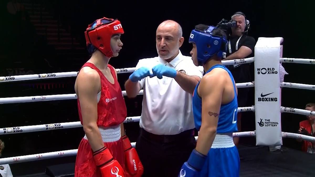 Dwie bokserki w kaskach i rękawicach stoją naprzeciwko siebie na ringu, między nimi stoi sędzia.