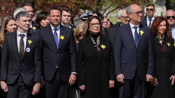 Uczestnicy uroczystości rocznicowych, w tym politycy, stojący razem, niekt&oacute;rzy z przypiętymi ż&oacute;łtymi żonkilami.