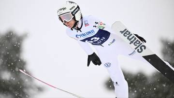 Skoczek narciarski w białym kombinezonie i kasku podczas skoku.