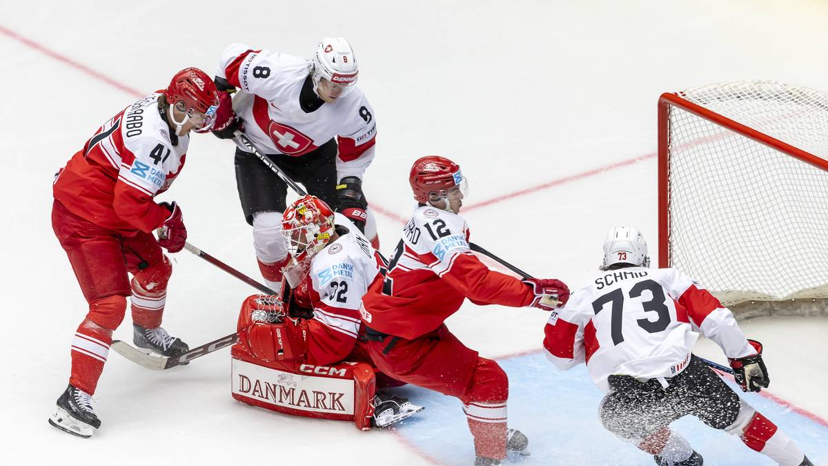 Pięciu zawodnik&oacute;w drużyny hokejowej w czerwono-białych strojach rywalizuje o krążek z zawodnikiem w białym stroju z numerem 73 na plecach. Dw&oacute;ch graczy jest blisko bramki, a jeden upada na l&oacute;d.
