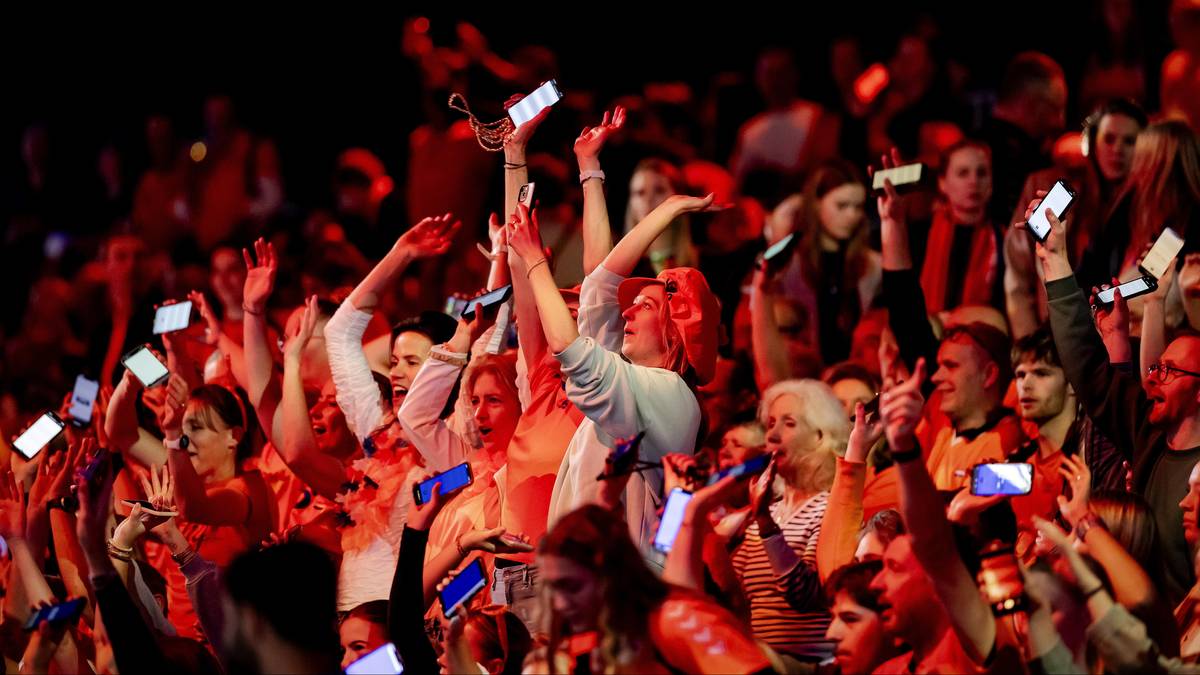 Tłum ludzi w pomieszczeniu, wielu z nich trzyma telefony komórkowe z włączonymi ekranami.