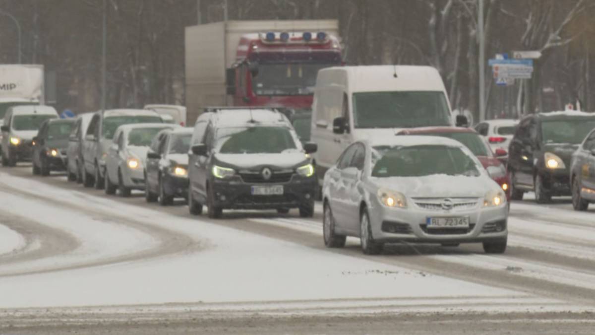 Korek samochod&oacute;w na zaśnieżonej drodze, widoczne r&oacute;żne typy pojazd&oacute;w, w tle ciężar&oacute;wki.