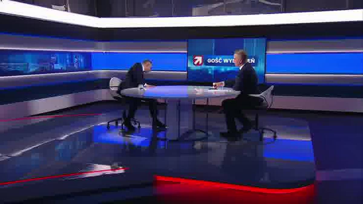 Dw&oacute;ch mężczyzn w garniturach siedzi przy stole w studiu telewizyjnym.