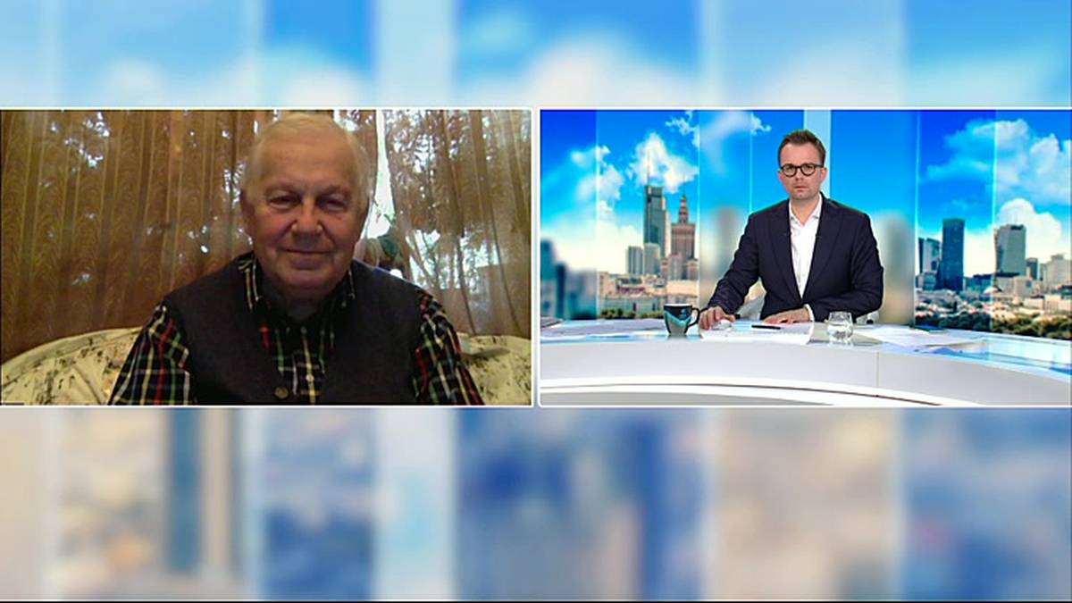 Dw&oacute;ch mężczyzn w rozmowie. Po lewej starszy mężczyzna siedzi w pomieszczeniu, po prawej młodszy mężczyzna siedzi przy stole w studiu telewizyjnym na tle panoramy miasta.