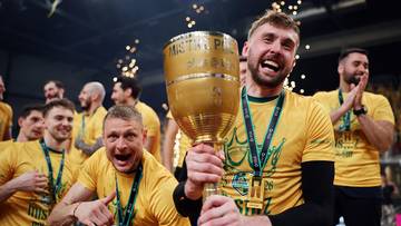 Radośni sportowcy w ż&oacute;łtych koszulkach świętujący zwycięstwo, jeden z nich trzyma duży złoty puchar.